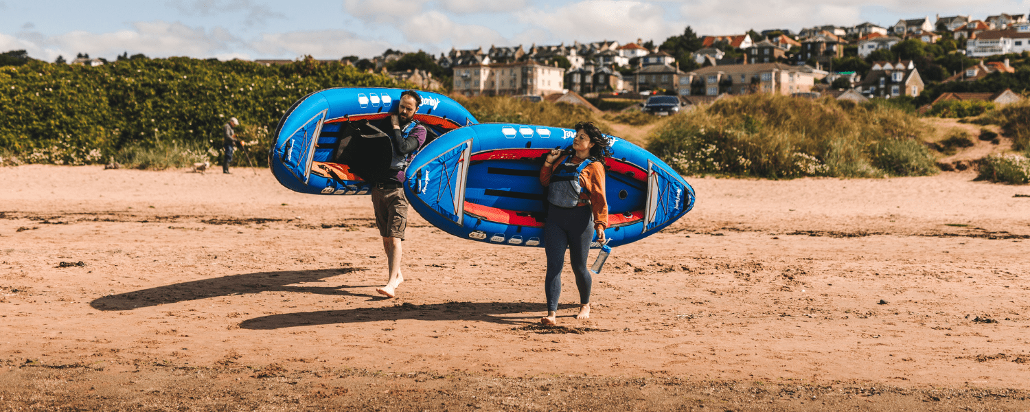 two kayakers walking across the beach with their inflatable kayaks on their shoulders