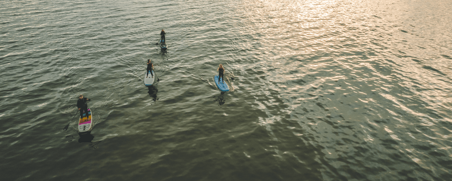 an aerial photo of a group of paddle boarders on the sea as the sun sets behind them