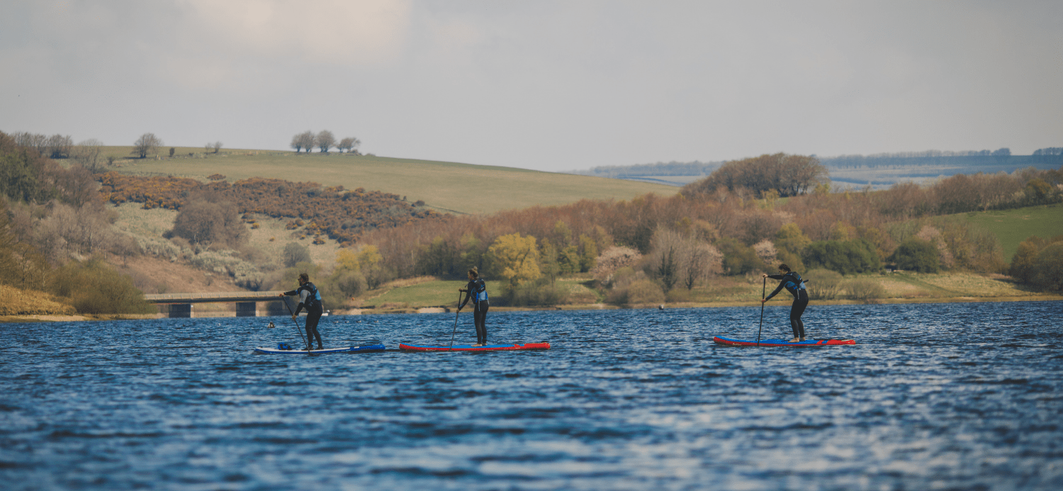 Group of people stand up paddleboarding on a lake in the UK