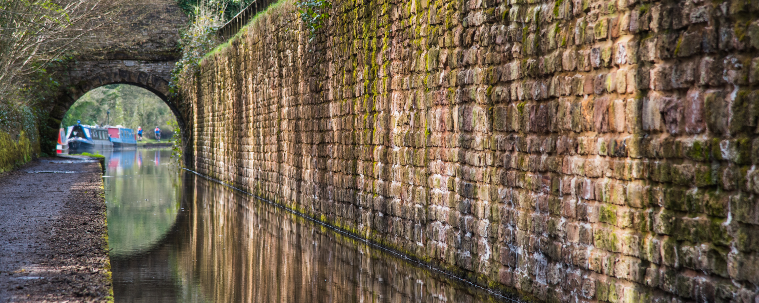 peak forest canal reflecting sunlight onto the high stone brick wall opposite the footpath