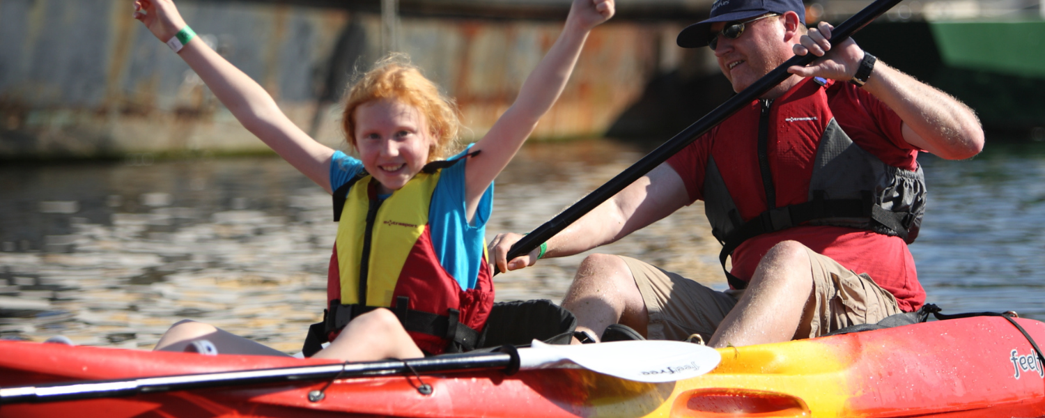 dad and daughter on a kayak while daughter cheers