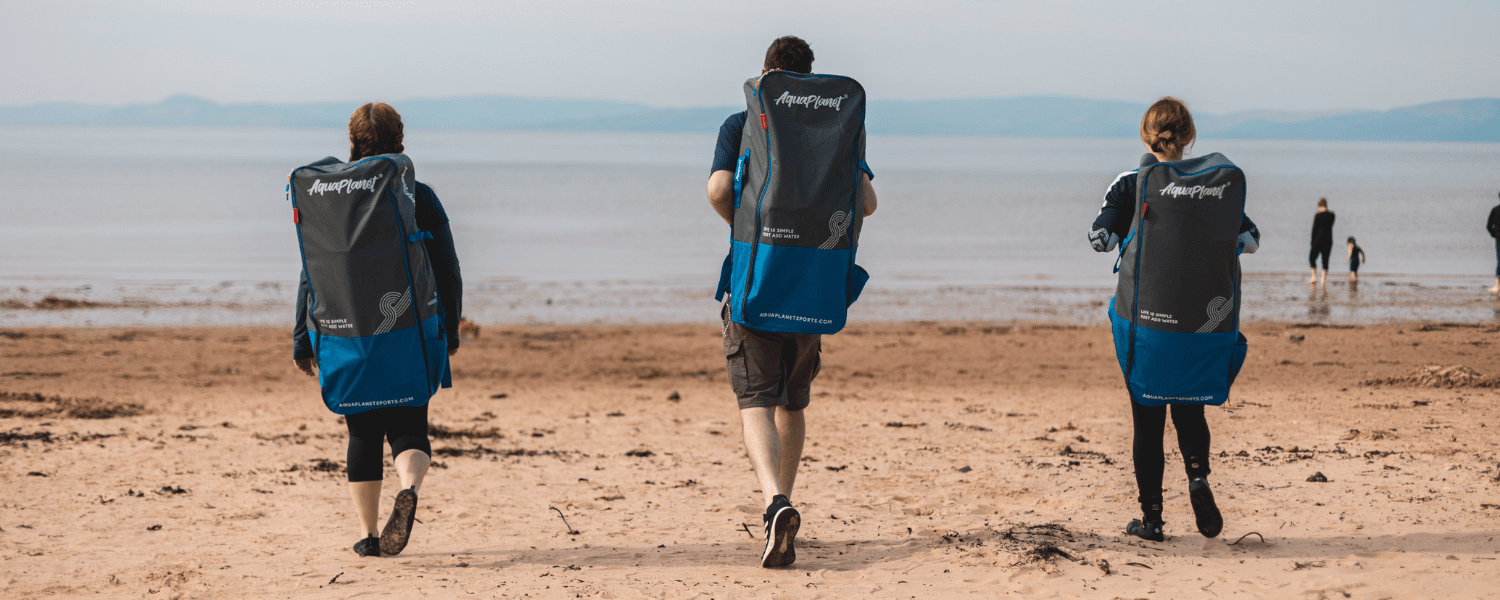 group of people walking towards the water with paddle boards on their backs