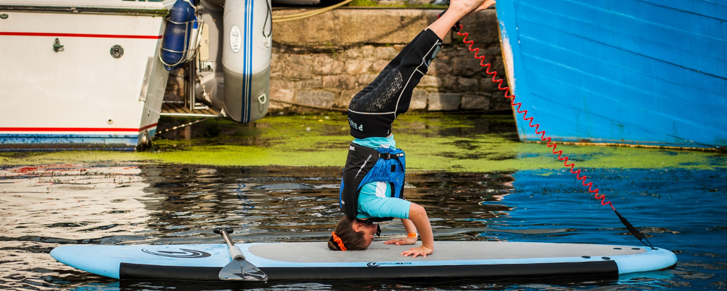 woman doing a head stand on a paddle board while on the water