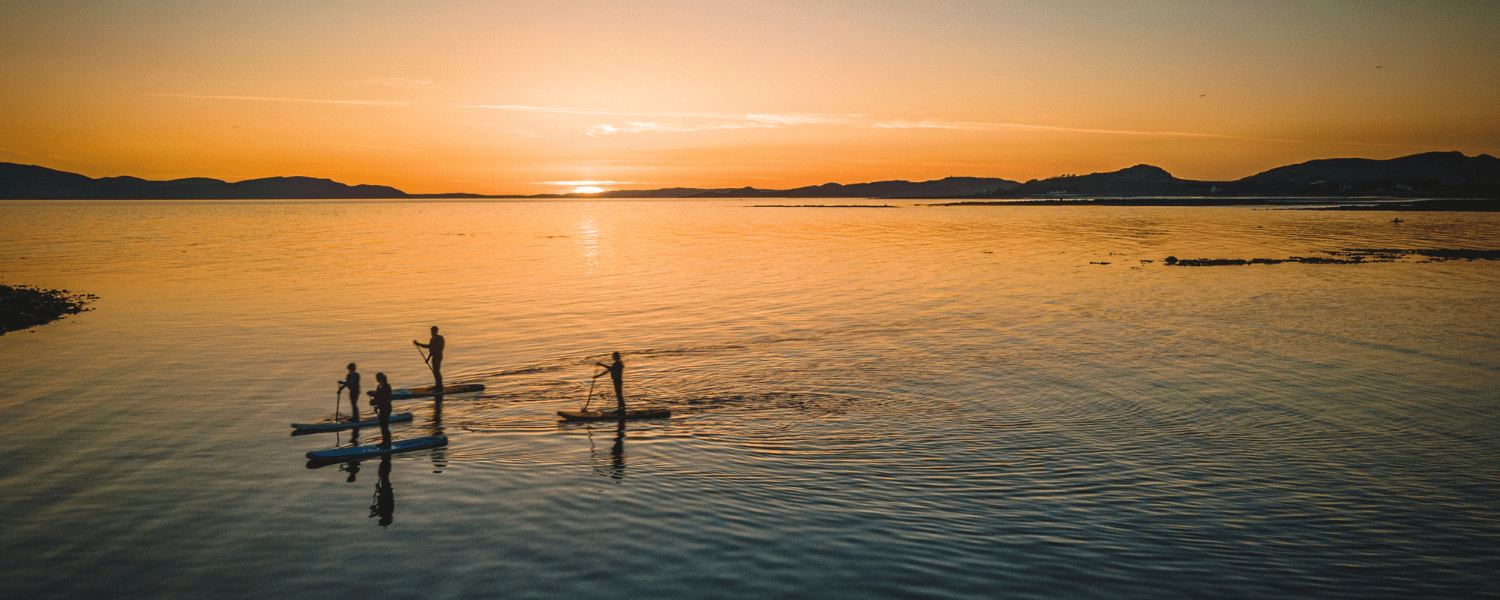 group of people paddling on a calm lake at sunset