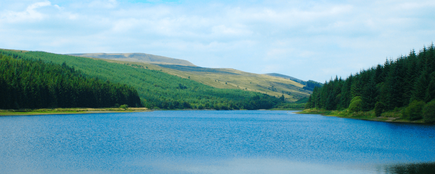 a large calm lake with a very green hill overlooking it