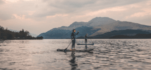 two women paddle boarding on a lake with some hills in the background