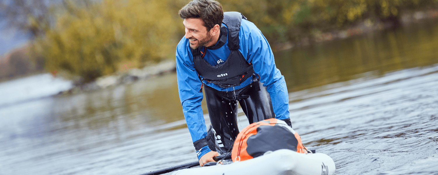 a man on a paddle board on his knees wearing a buoyancy aid