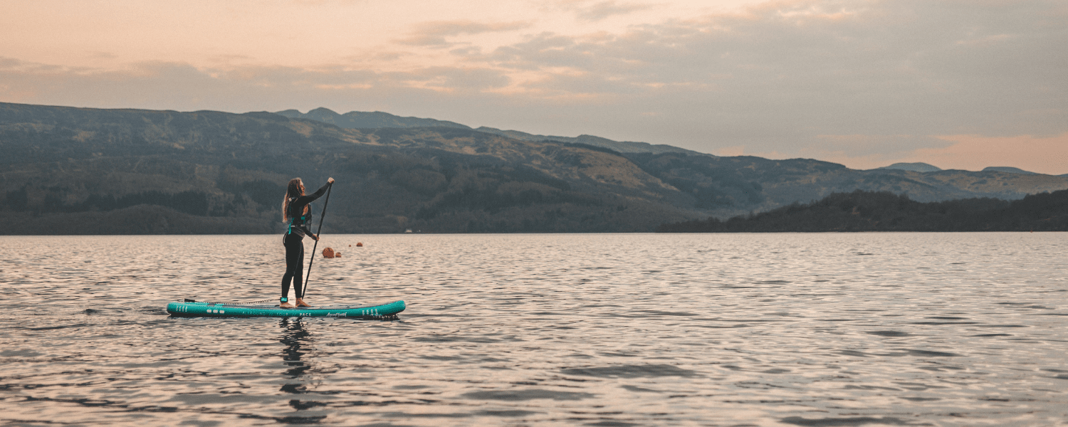 a solo paddle boarder on a lake with a large hill behind her