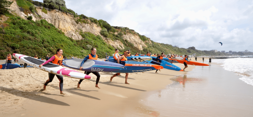 a group of sup racers sprinting from the beach into the sea