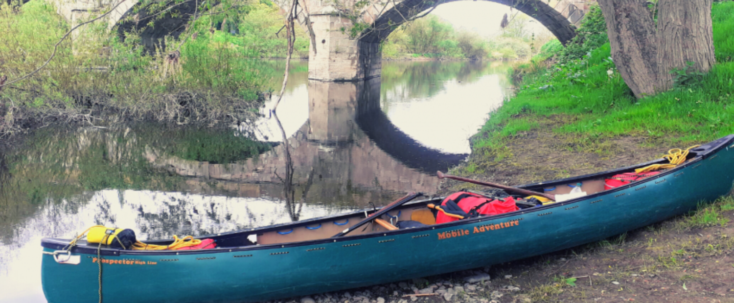 The canoe loaded up on the river bank below a bridge