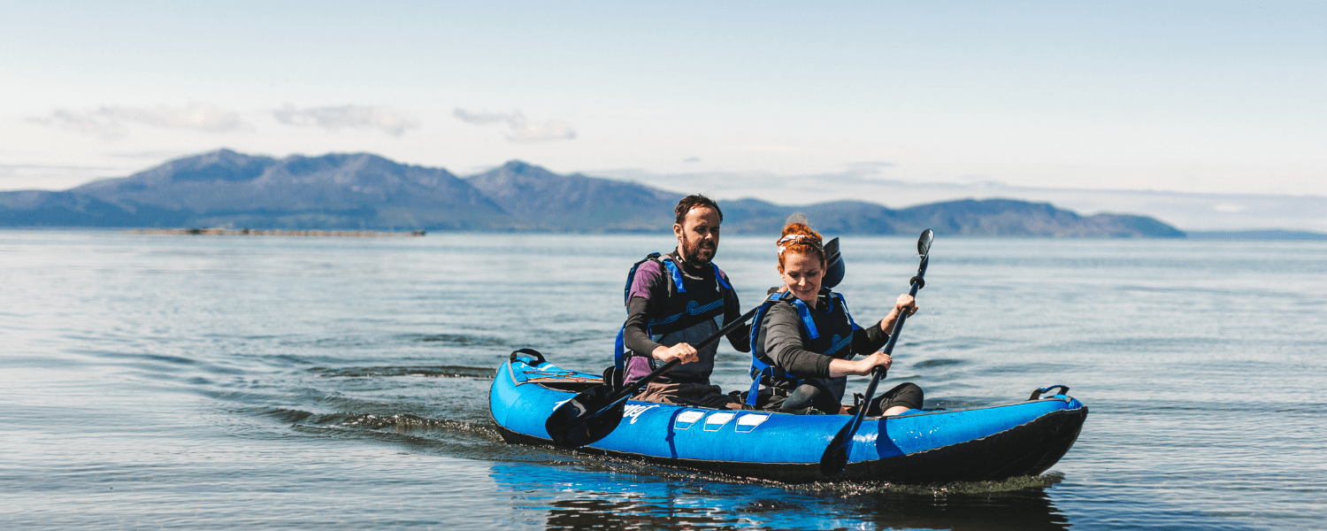 two people in an inflatable kayak with mountains in the background