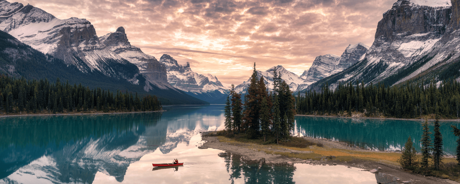 a solo canoeist on a last surrounded by epic mountains