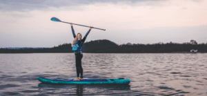 Woman on a paddle board with paddle above her head and big smile