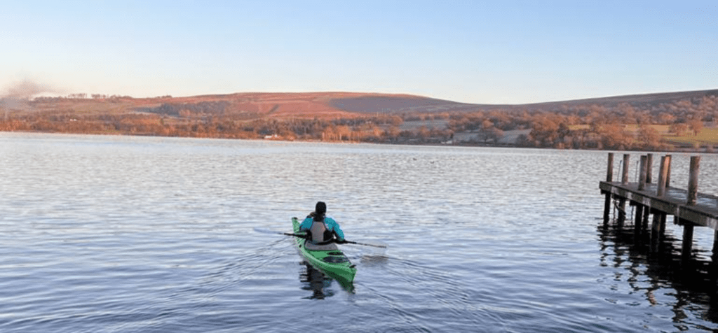 Saira Is-Haq paddling onto a lake with hilly surroundings