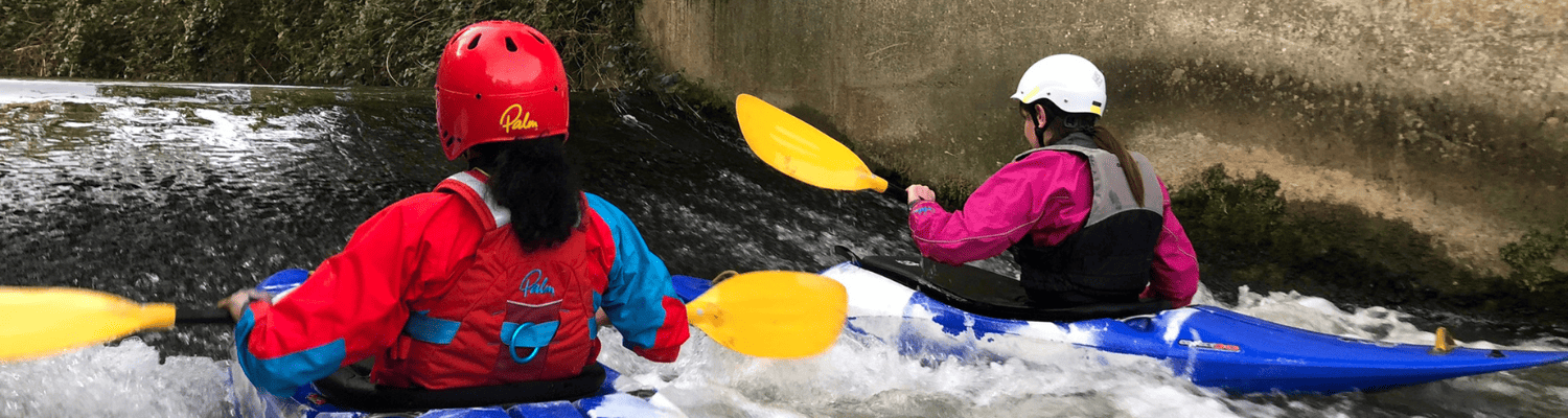 pair of british canoeing members surfing a wave