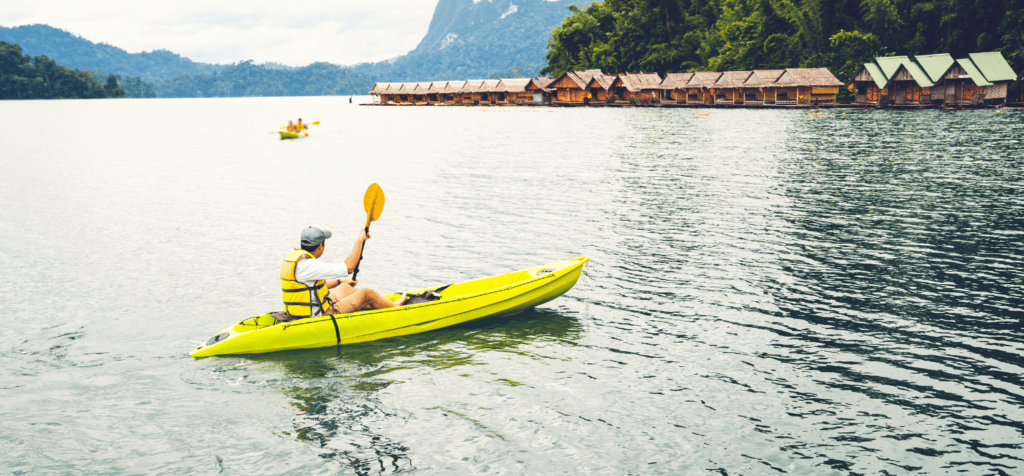 man on a sit on top kayak on the water looking at shacks and hills