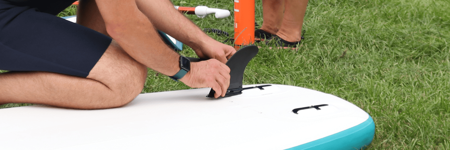 person attaching a fin to a paddleboard