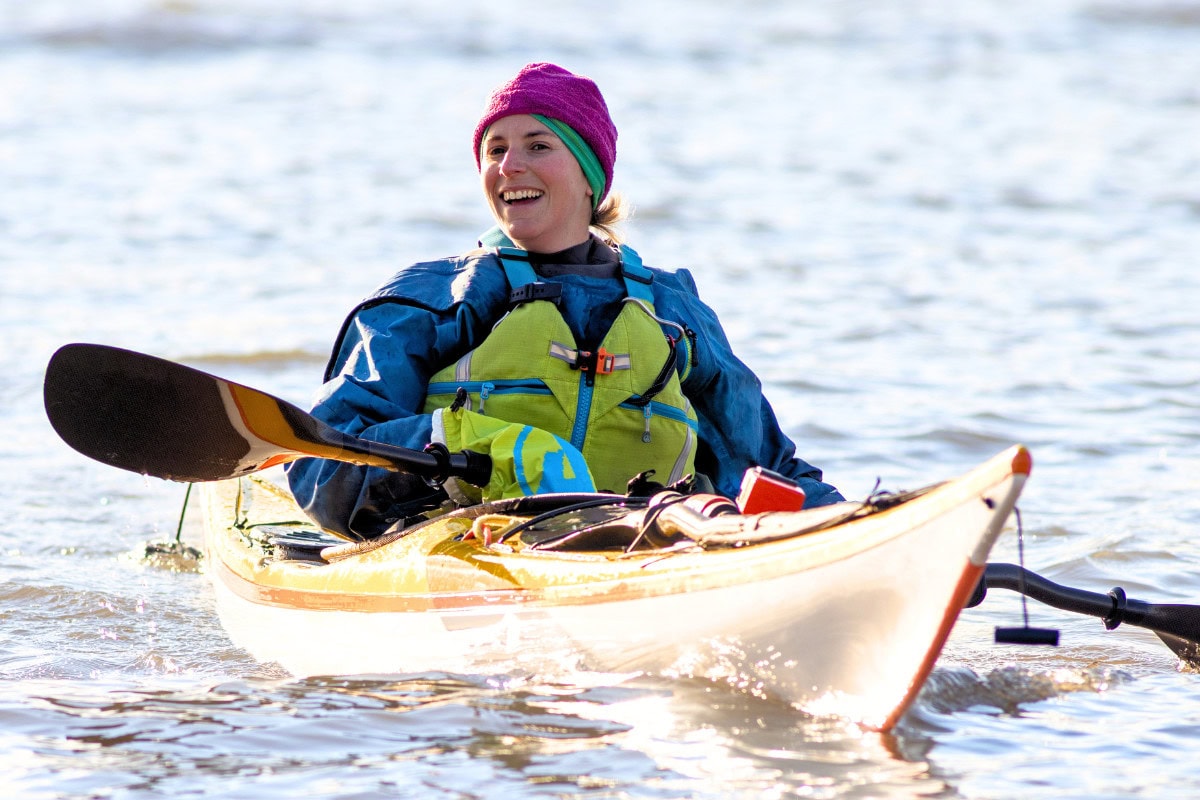 Female sea kayaker in autumn paddling kit. Wearing pogies, waterproof cag, buoyancy aid and thermal hat.