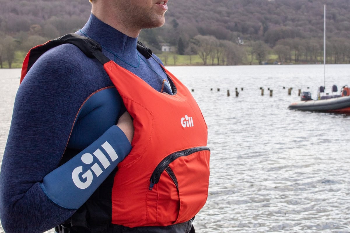 Man next to a lake getting ready to go paddling wearing a thermal base layer and buoyancy aid