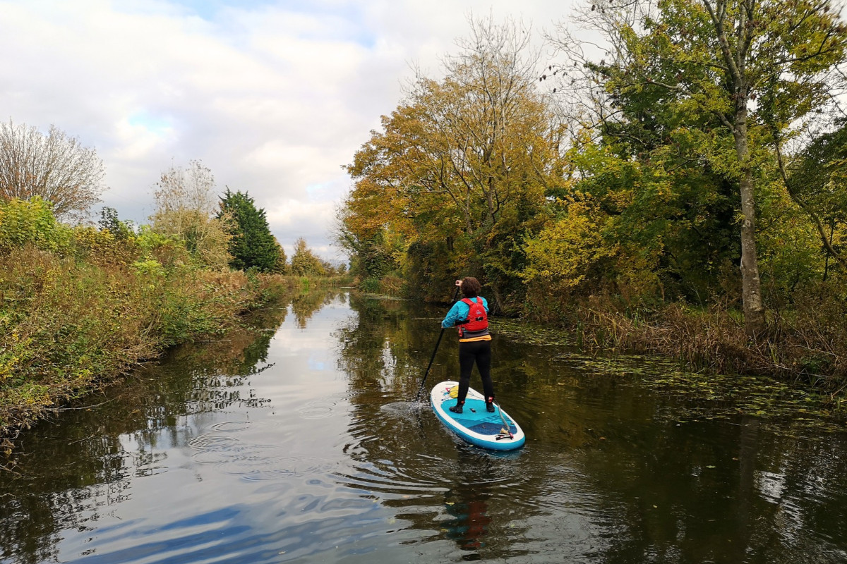 Paddleboarder on the Lancaster Canal in autumn. Colourful autumnal trees line the canal.